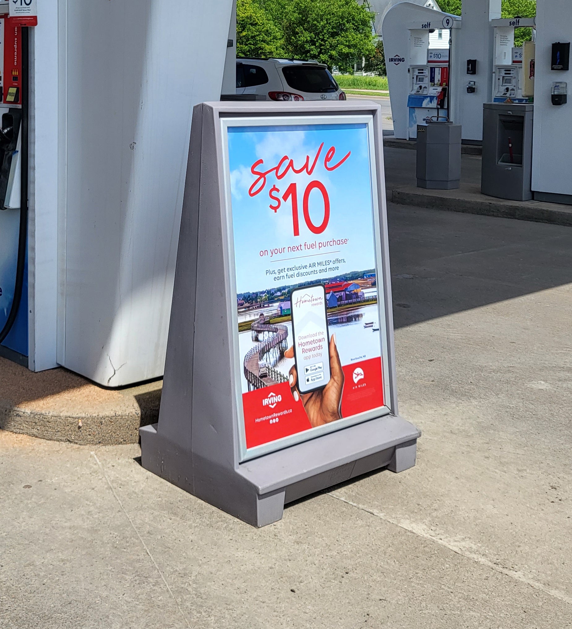 Gorrie RCP outdoor A-Board sign stand at an Irving gas station. The durable, grey plastic promotional display features a 'Save $10' fueling rewards advertisement, illustrating high-visibility retail signage solutions.